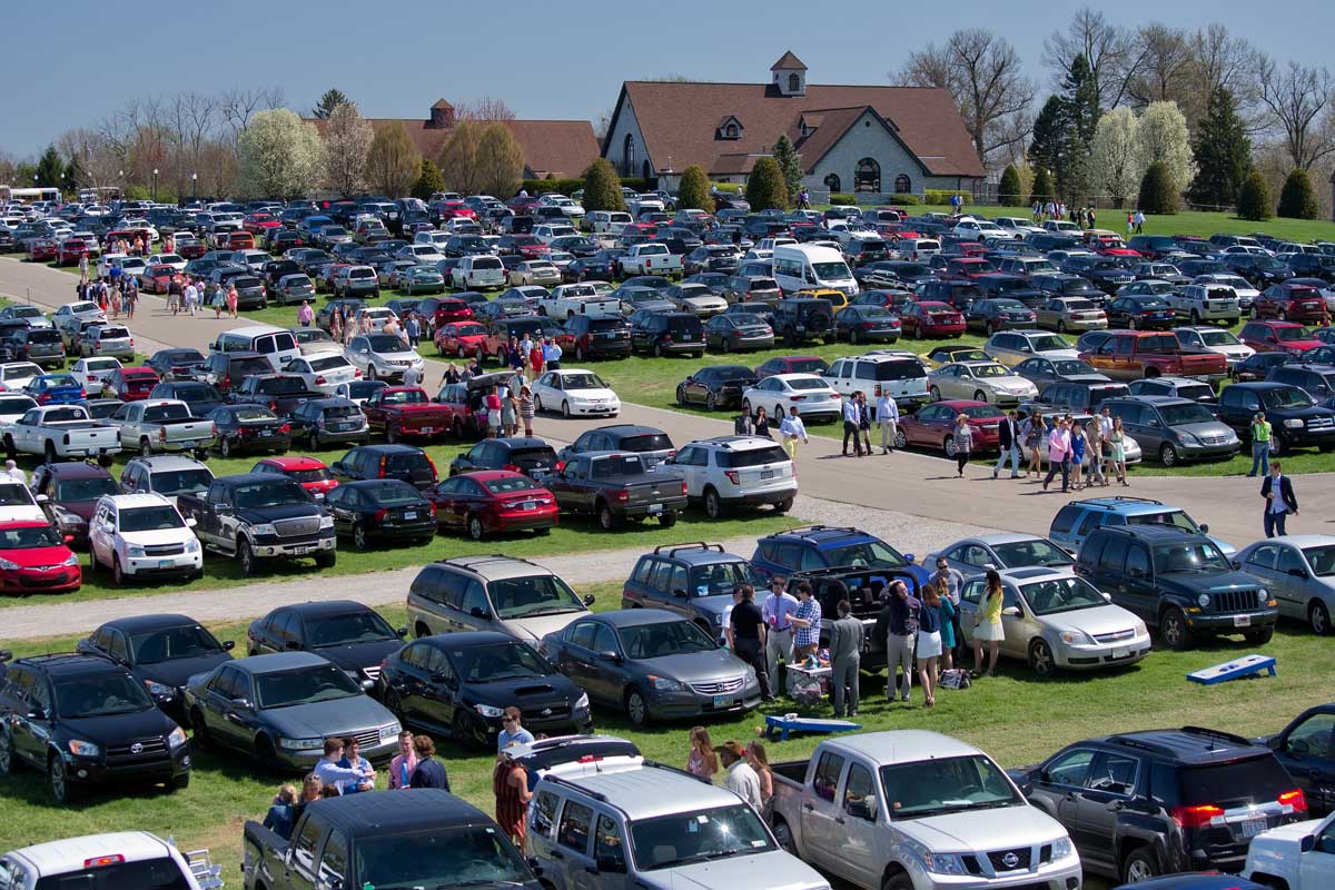 Photo of cars parked in a field. There are people tailgating and moving to and from the Keeneland facilities.